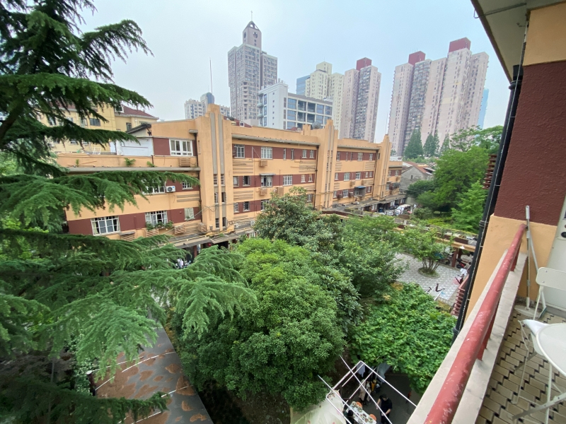 从常哲晖家的阳台看建安公寓第二排楼全景，两栋楼之间有个面积很大的院落，有连廊连接。一楼还有人支起桌子露天吃饭。佟鑫摄