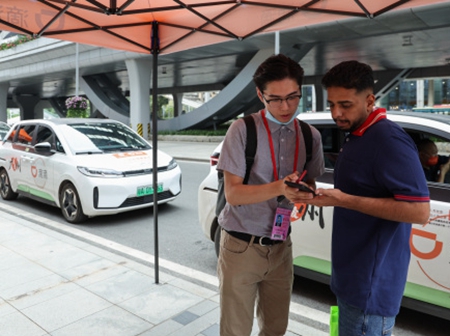 一位外国客商在服务人员帮助下学习使用网约车打车软件。新华社资料